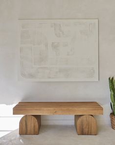 a wooden bench next to a potted plant in front of a painting on the wall