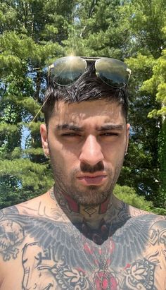 a man with tattoos and sunglasses on his head looking at the camera while standing in front of some trees