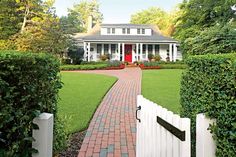 a white house with a red door and brick path leading to the front yard area