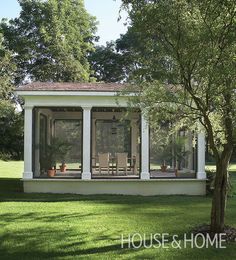 a small white house sitting on top of a lush green field next to a tree