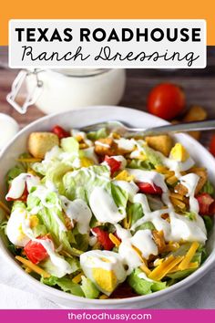 a white bowl filled with lettuce, tomatoes and ranch dressing on top of a table