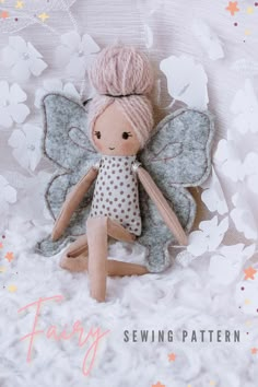 a doll with pink hair sitting on top of a white blanket next to flowers and butterflies