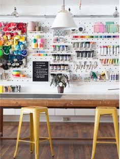 two yellow stools in front of a table with sewing supplies on the wall behind it