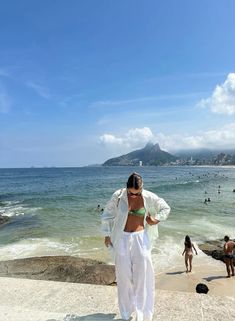 a woman standing on top of a sandy beach next to the ocean with people swimming in the water