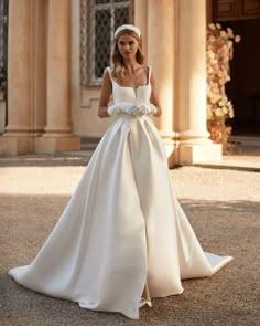 a woman in a white wedding dress is standing on the ground with her hands behind her back