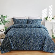 a bed with blue and green bedspread in a white room next to a potted plant