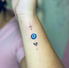 a woman's arm with a cross and evil eye tattoo on the left wrist