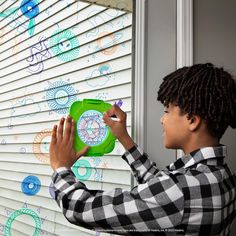 a young boy drawing on the window sill with colored chalks and a green clock