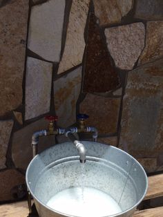 a metal bucket filled with water sitting on top of a wooden table next to a stone wall