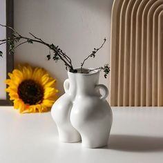 two white vases sitting on top of a table next to a yellow sunflower