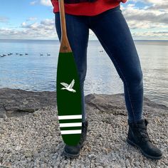 a woman standing on the beach holding a green and white surfboard with an eagle painted on it