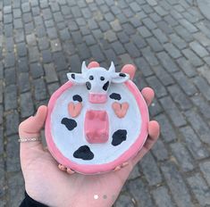 a hand holding a small ceramic cow on it's side in front of a brick road