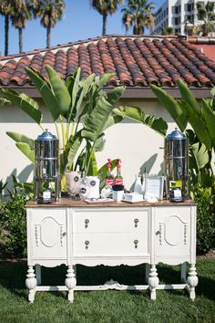 a table with two silver vases on top of it in front of some palm trees