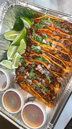 a tray filled with tacos and sauces on top of a table next to lime wedges