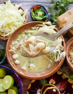 a spoon full of soup sitting on top of a table next to bowls filled with food