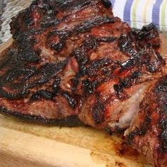 two pieces of meat on a cutting board next to a fork and knife with a striped napkin