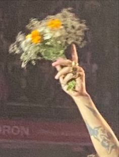 a person holding flowers up in the air with one hand and two fingers raised above them