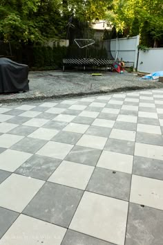 a large checkered tile patio in the middle of a yard with trees and bushes