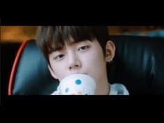 a young man sitting in a chair drinking out of a white cup with blue dots on it