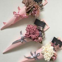 three pink paper cones with flowers and ribbons tied to each other on a white surface