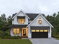 a white two story house with black garage doors and lights on the windows at night