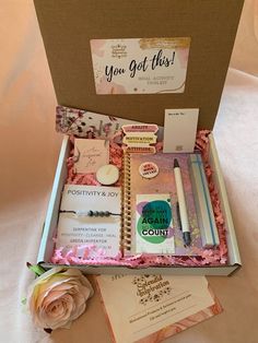 an open box containing personal items on a white sheeted surface with a rose and notepad