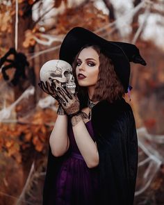 a woman in a witch costume holding a skull and wearing a black hat with her hands