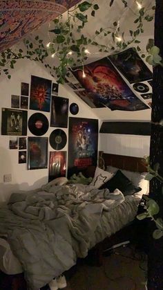 an unmade bed in a room with pictures on the wall and plants hanging from the ceiling