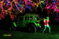 a green jeep with lights in the background and a person dressed as grinen standing next to it