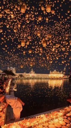 many lanterns floating in the air over water at night with people sitting on benches and watching them