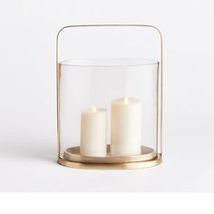 three white candles in a glass container on a metal stand with a gold ring around it