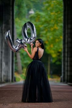 a woman in a black dress holding two silver balloons that spell out the word love