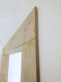 a wooden frame on the wall next to a white wall with a mirror in it