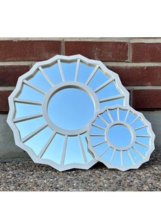 a mirror sitting on the ground next to a brick wall with a circular design in it