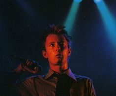 a man holding a microphone in front of two blue and green spotlights on a stage