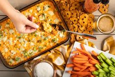 a person scooping food from a casserole dish with carrots and celery