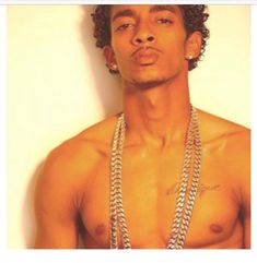 a shirtless young man with two chains around his neck and one chain on his chest