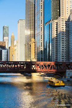 a yellow boat is on the water in front of some tall buildings and a bridge