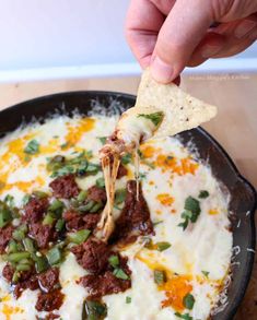 a hand holding a tortilla chip over a bowl of cheese and chili dip