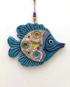 a blue fish is hanging from a wall with beads on it's head and eyes