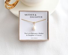 a mother and daughter necklace in a box on a white table with a gold bracelet