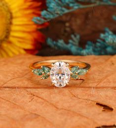 an oval shaped diamond ring with three leaves on the side, and a sunflower in the background