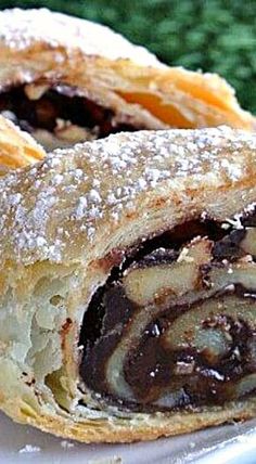 two pastries on a plate with powdered sugar and chocolate fillings, one cut in half