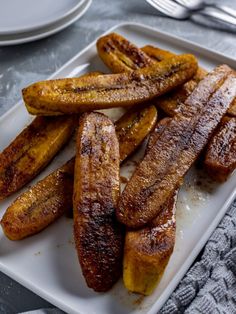 some bananas are sitting on a white plate with powdered sugar and silverware in the background