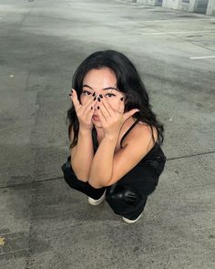 a woman is covering her face with her hands while sitting on the ground in an empty parking lot