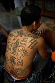 a man sitting on the ground with tattoos on his back