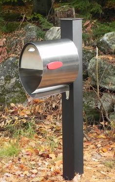 a mailbox in the middle of a field with leaves on the ground and rocks behind it