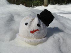 a knitted hat with a face on it laying in the snow next to trees