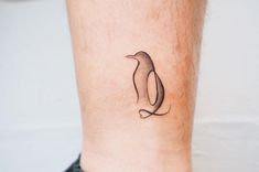 a small penguin tattoo on the ankle is shown in black and grey ink, with an outline of a penguin