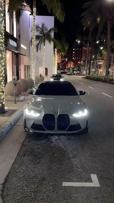 a white sports car parked on the side of a street at night with palm trees in the background